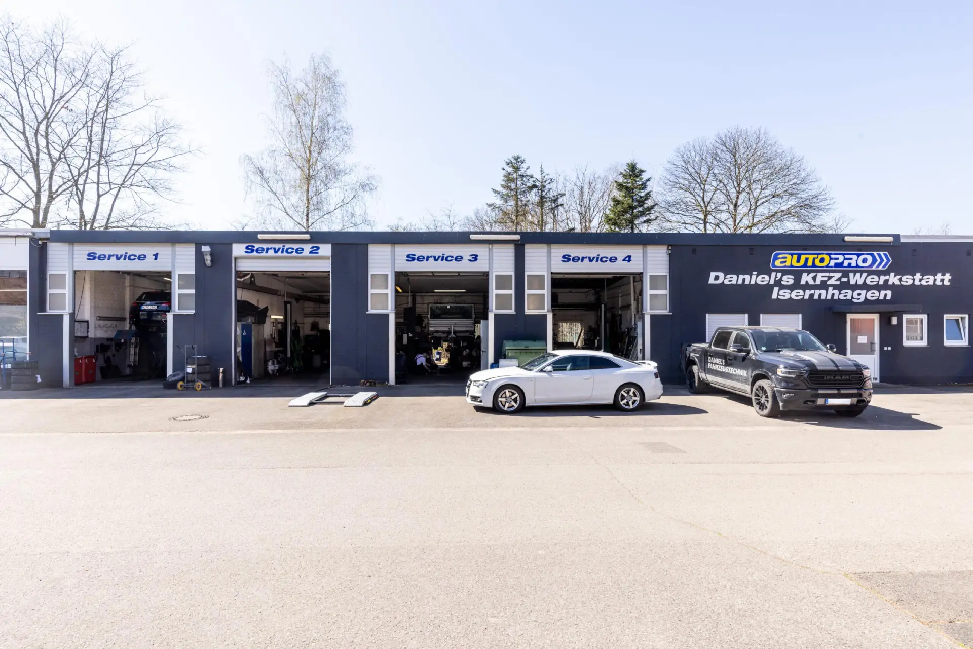 Außenansicht einer Kfz-Werkstatt mit vier Serviceboxen und zwei Autos davor.